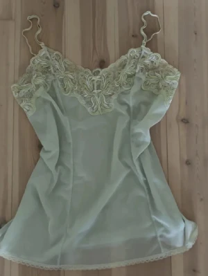 Ljusgrönt nattlinne med spetsdetaljer - Sött ljusgrönt linne med tunna axelband och vacker spets i samma ton över bysten. Materialet är tunt och lätt, vilket ger en luftig känsla. Perfekt för sommaren