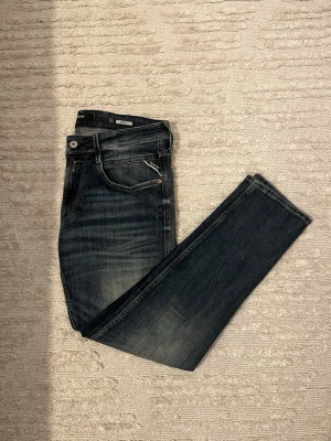 Mörkblå slim fit jeans från replay  - Säljer ett par mörkblå slim fit jeans från replay  med snygga slitningar och klassiska fem fickor. Jeansen har dragkedja och knapp i midjan samt diskreta detaljer på fickorna. Perfekta för en avslappnad och trendig look.
