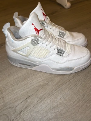 Jordan 4 oreo  - Snygga Air Jordan 4 Retro sneakers i vitt läder med meshpaneler och detaljer i grått. Klassisk siluett med högt skaft och röd Jumpman-logga på plösen. Sulan har gråa stänk och skon har ikoniska plastdetaljer vid snörningen. Perfekta för dig som gillar streetwear.