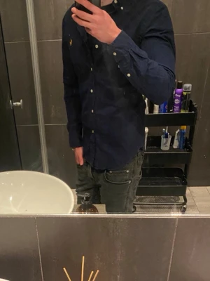 Mörkblå skjorta från Ralph Lauren som känns som en S - Snygg mörkblå skjorta från Ralph Lauren med klassisk krage och knappar framtill. Skjortan har lång ärm och den ikoniska broderade loggan på bröstet. Perfekt för en stilren look.