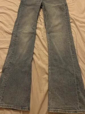 Ljusblåa utsvängda jeans - Säljer ett par ljusblå jeans med utsvängda ben och klassisk femficksdesign. Jeansen har en vintage tvätt och är tillverkade i denim. Perfekta för dig som gillar retrostil och vill ha ett par bekväma och snygga jeans. Helt oanvänd.