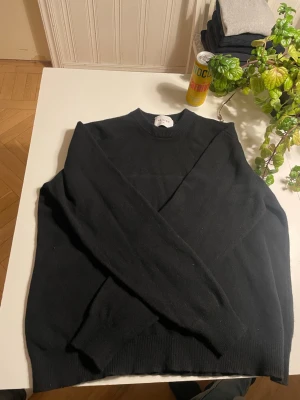 Svart merinoullströja från Vailent - Snygg svart stickad tröja från Vailent i mjuk merinoull. Tröjan har rund halsringning, långa ärmar och ribbstickade muddar. Perfekt för dig som gillar stilrena och bekväma plagg med en klassisk look. Krymt i storleken så den är Large.