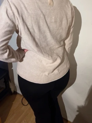 Beige stickad tröja med mönster - Beige stickad tröja med diskret rutmönster framtill och ribbade muddar vid ärmslut och nederkant. Tröjan har rund halsringning och är i mjukt material, perfekt för lager-på-lager-stil.