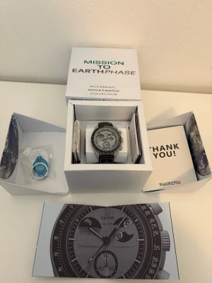 Omega x Swatch Mission to Earthphase - Snygg klocka från Omega x Swatch Bioceramic MoonSwatch Collection, modell Mission to Earthphase. Klockan har en rund urtavla i grått och svart med tydliga visare och detaljer. Kommer i originalförpackning med tillbehör och cool design.