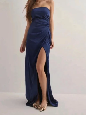 Marinblå axelbandslös långklänning - Snygg marinblå långklänning med axelbandslös design och hög slits framtill. Klänningen har en omlott-look och smickrande passform som framhäver siluetten. Perfekt för dig som vill sticka ut med en elegant och modern stil.