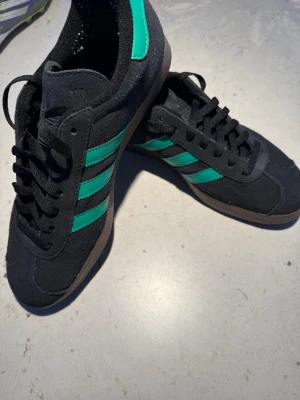 Adidas Gazelle svarta/gröna - Säljer mina Adidas Gazelle svarta med gröna detaljer. För små för mig och har bara testat dem, så de är i nytt skick. Köpta för 1350kr. Hör av dig vid frågor!