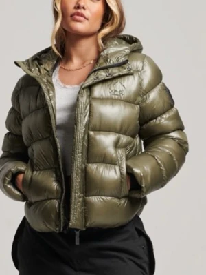 Olivgrön dunjacka - Säljer en olivgrön pufferjacka från superdry med glansigt material och stor huva. Jackan har dragkedja framtill och två sidofickor. Perfekt för kalla vinterdagar. Helt slutsåld!! Så snygg! Nypris 1500