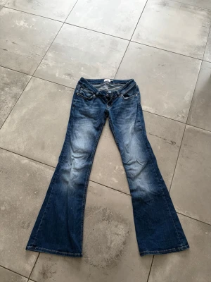 Blå bootcut jeans från 157 - Snygga blå bootcut jeans från 157 med kort längd.Väldigt bra skick är bara andvända en gång. Jeansen har slitningar och ljusare partier framtill för en cool, använd look. Klassisk femficksmodell med dragkedja och knapp. Perfekta för dig som gillar retrovibbar och bekväm passform.