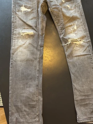 Grå slitna jeans från Replay - (Pris kan diskuteras)! Säljer ett par grå jeans från Replay med slitningar och hål på både lår och knän. Jeansen har en smal passform och klassisk femficksdesign. Snyggt tvättade detaljer och trendigt distressed look. Perfekta för dig som gillar en avslappnad och edgy stil. Med en lagning i skrevet som man inte ser på. Därför d låga priset 