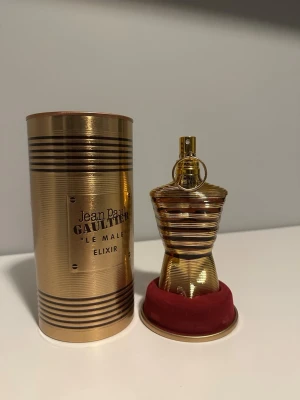 Jean Paul Gaultier Le Male Elixir - Lyxig parfym från Jean Paul Gaultier, Le Male Elixir. Flaskan har en unik kroppsliknande form i glänsande guld med horisontella ränder. Kommer med en matchande guldfärgad cylinderförpackning och röd sammetsbas. Perfekt för dig som gillar exklusiva dofter.