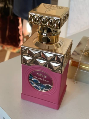 Paris Corner Caramel Dulce parfym - Lyxig parfymflaska från Paris Corner, modellen Caramel Dulce. Flaskan är fyrkantig med en matt rosa kropp och detaljer i guld, inklusive ett dekorativt lock med geometriskt mönster. Märkets logga och namn syns på flaskan. Perfekt för dig som gillar snygg design. Testat max 5 spray!