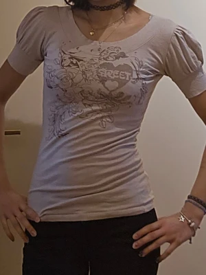 Ljusbeige topp med puffärm och tryck - ❗️Skriv innan köp❗️ ljusbeige topp med puffärmar och ett stort tryck med hjärta och blommor framtill. Tight passform och rund halsringning. Taggen är lite skadad så vet inte var den kommer från. Har fått secondhand.