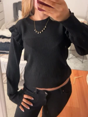 Svart ribbad tröja med puffärm - Trendig svart ribbad tröja med puffärmar och rund halsringning. Croppad modell som ger en snygg siluett. Perfekt att matcha med höga jeans för en cool look. Materialet ser mjukt och stretchigt ut.