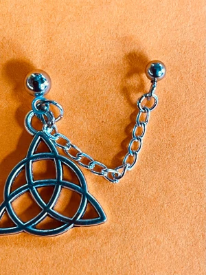 By prisförslag- 1 st Silvrigt örhänge med keltisk knut - Ett coolt silvrigt örhänge med keltisk knut-design. Örhänget har en kedja och rund plupp upptill, vilket ger en edgy och unik look. Perfekt för dig som gillar detaljer och stilrena smycken.