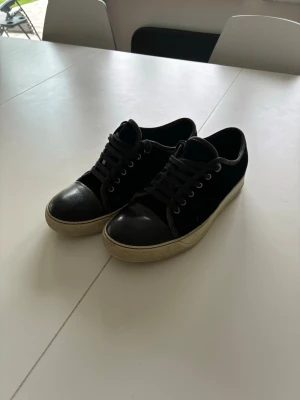 Lanvins Marinblå - Stilrena mörkblå Lanvins med ovandel i mocka och tåparti i blankt skinn. Skorna har vita sulor och matchande mörkblå snören. Perfekta för en clean och avslappnad look. 