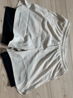 Vita träningsshorts med Quickdry - Vita träningsshorts med svart innerbyxa och Quickdry Technology-tryck på sidan, från Lager 157. Shortsen har elastisk midja och är perfekta för dig som vill ha bekväma och funktionella shorts till träningen.