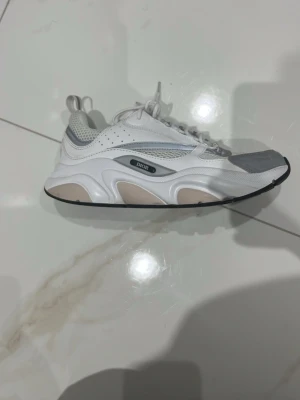 Vita och grå sneakers - Snygga sneakers från  i vitt och grått med meshpaneler och detaljer i läder. Skorna har en chunky sula i vitt och beige samt logga på sidan. Klassisk snörning och dragflikar bak för enkel påtagning. Perfekta för dig som gillar exklusiv streetwear.