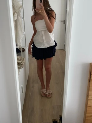 Mörkblå volangkjol i kort modell - Supersöt mörkblå kortkjol med volangdetaljer och loose passform. Kjolen har en flowy känsla och passar perfekt till sommaren. Ingen synlig logga eller märke, men materialet känns som tunn bomull eller polyester.