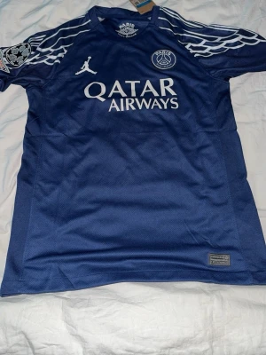 PSG matchtröja O. Dembélé #10 blå - Snygg blå PSG matchtröja med O. Dembélé och nummer 10 på ryggen. Tröjan har vita detaljer, Qatar Airways-logga på bröstet och Champions League-märke på ärmen. Tillverkad i lätt och ventilerande funktionsmaterial, perfekt för fotboll eller träning.