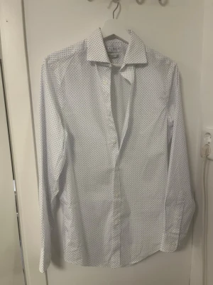 Vit skjorta från Lauren Ralph Lauren - Snygg vit skjorta från Lauren Ralph Lauren med diskret blått mönster. Den är sparsamt använd och i mycket bra skick.