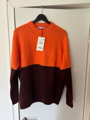 Tvåfärgad stickad tröja från Zara - Säljer en snygg stickad tröja från Zara i storlek L. Tröjan har en cool färgblock-design med orange upptill och mörkbrunt nedtill. Rund halsringning och mjukt material som känns skönt mot huden. Perfekt för dig som vill sticka ut lite extra.