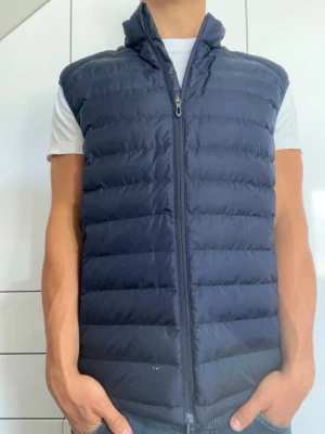 Mörkblå dunväst - Mörkblå dunväst från okänt märke. Strl vet ej men skulle gissa Large. Finns liten vit fläck på framsidan vid midjan (se bild 1). Modellen är 178 cm och väger 77 kg. Hör gärna av dig vid frågor!