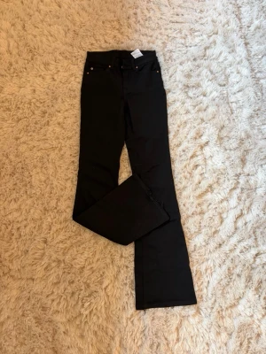 Svarta bootcut jeans med hög midja - Säljer ett par svarta bootcut jeans med medelhög midja och klassisk femficksdesign. Jeansen har utsvängda ben och stängs med dragkedja och knapp. Perfekta för dig som gillar en tidlös och trendig look. Mycket fint skick! Storlek xs/32