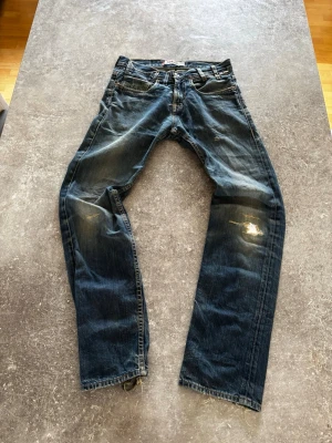 Levis vintage washed straight/bootcut - Säljer ett par klassiska blå Levi's jeans med raka ben och slitningar på knäna samt fransiga benslut. Jeansen har fem fickor och en vintage tvättad look. Perfekta för en avslappnad och trendig stil.