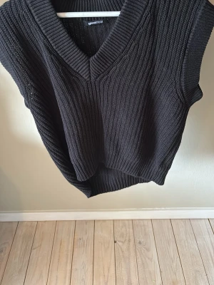 Svart stickad väst från Gina Tricot - Snygg svart stickad väst från Gina Tricot med v-ringad hals och bred ribbad kant. Perfekt att bära över en skjorta eller t-shirt för en trendig lager-på-lager-look. Västen har en loose passform och är riktigt mjuk och bekväm.