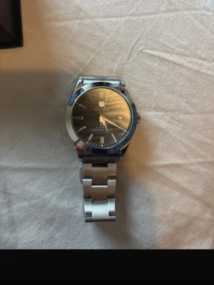 Silverfärgad automatisk klocka Benyar - Stilren automatisk klocka från Benyar med silverfärgat armband i metall och mörk urtavla. Klockan har klassisk rund form, tydliga index och synlig mekanism på baksidan. Perfekt accessoar för dig som gillar tidlös design och kvalitetskänsla.