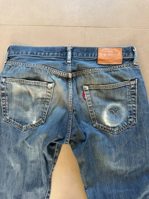 Blå raka jeans från Levi's - Klassiska blå jeans från Levi's med raka ben och slitningar på bakfickorna. Jeansen har fem fickor, läderpatch bak i midjan och den ikoniska röda Levi's-lappen på ena bakfickan. Tillverkade i denim med en snygg tvättad look. Levis 501 w31 l34