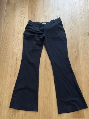 Lågmidjade svarta bootcut kostymbyxor från Weekday - Snygga svarta kostymbyxor från weekday med bootcut passform och låg midja. Byxorna har klassisk design med diskret knapp och dragkedja framtill. Tillverkade i ett mjukt och följsamt tyg som ger en stilren look.