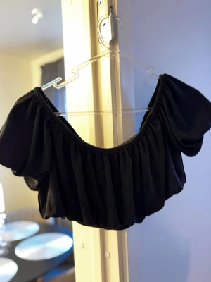 Svart off shoulder topp med puffärm - Trendig svart off shoulder croptopp med puffärmar. Tunt, mjukt tyg som ger en luftig känsla och snygg siluett. Perfekt för att skapa en cool och avslappnad look.