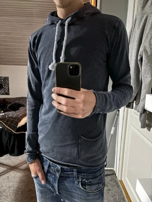 Hoodie - Snygg mörkblå hoodie med huva och vita, grova dragsnören. Hoodien har en liten ficka framtill och är tillverkad i ett mjukt, tunt material. Perfekt för en avslappnad och stilren look.