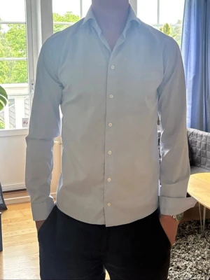Eton skjorta  - Säljer en stilren skjorta med klassisk krage och knappar framtill. Skjortan har lång ärm och en slim passform, perfekt för dig som gillar en clean och enkel look. Tillverkad i bomull för en skön känsla hela dagen.