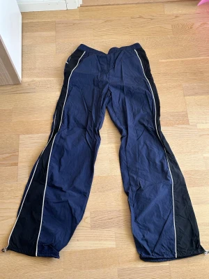 Blå träningsbyxor med vita detaljer - Snygga träningsbyxor i mörkblått. Byxorna har raka ben och dragsko vid benslut för justerbar passform. Perfekta för sport eller chill.