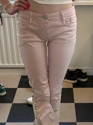 Ljusrosa jeans med spetsdetaljer - Säljer ett par ljusrosa jeans med snygga spetsdetaljer längs benen. Jeansen har klassisk femficksmodell, normal midja och raka ben. Materialet är mjukt och stretchigt för extra komfort. Perfekta för dig som vill ha en unik och trendig look💕💕💕.