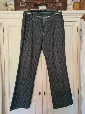 Ljussvart randiga bootcut jeans - Säljer ett par ljussvarta jeans med vita smala ränder och bootcut-modell. Jeansen är midwaist och stängs med knapp och dragkedja. Snygg klassisk retrostil som passar perfekt till sneakers eller boots. Storlek 42/44. Hör gärna av dig vid frågor😁