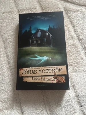 Lockfågeln av Jonas Moström - Spännande deckare av Jonas Moström med svart och mystisk framsida. Boken handlar om psykiatern Nathalie Svensson och kriminalkommissarie Johan Axberg som utreder mord i Umeå. Pocketbok med omslag i papper och tryckt text.