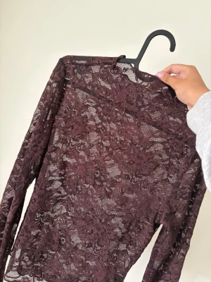 Brun spetsblus med lång ärm - Säljer en brun långärmad blus i genombruten spets med blommigt mönster. Perfekt för dig som vill ha en elegant och trendig topp med transparent känsla. Passar snyggt till både jeans och kjol.