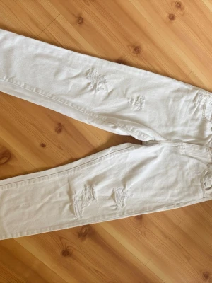 Vita mom jeans med slitningar - Säljer ett par vita mom jeans med trendiga slitningar på framsidan. Jeansen har hög midja, raka ben och klassiska bakfickor. Perfekta för en avslappnad och cool stil. Materialet är bomull som ger en skön känsla hela dagen.