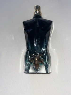 Le baue från Jean Paul Gaultier - Cool parfymflaska formad som en manlig torso i mörkblått glas med guldfärgad kork och metallisk detalj framtill. Flaskan har en unik och konstnärlig design som verkligen sticker ut på hyllan. Perfekt för dig som gillar snygga och ikoniska parfymer. Mer än halva kvar burken följer även med 