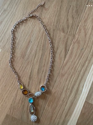 Äkta Swarovski halsband!! Jätte fin  - Unikt halsband med guldfärgad kedja och stora färgglada stenar i blått, gult och brunt. Dekorerat med vita pärlliknande detaljer och gnistrande stenar. Kedjan har justerbar längd och ett iögonfallande hängsmycke. Perfekt för dig som vill sticka ut.