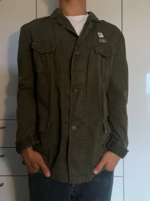 Olivgrön overshirt - Olivgrön overshirt från ett märke vid namn av Strellson Swiss cross. Inga tydliga defekter men definitivt använd. Modellen är 178 cm och väger 77 kg. Hör gärna av dig vid frågor!