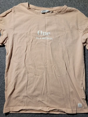 Ljusrosa t-shirt med tryck - Ljusrosa t-shirt från H&M med texten 'One in a million.' tryckt på bröstet. Klassisk rund halsringning och korta ärmar. Tillverkad i mjuk bomull för en skön känsla. Perfekt för en avslappnad och enkel stil.