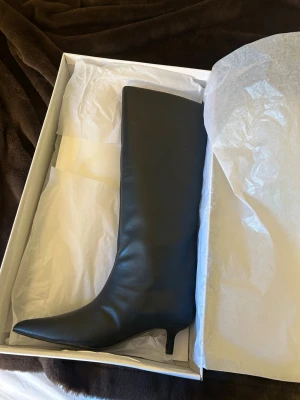 Svarta knähöga boots med smal klack - Säljer ett par svarta knähöga boots med spetsig tå och smal klack. Skorna har en stilren och elegant design i slätt material, perfekta för att lyfta vilken outfit som helst. Passar dig som gillar trendiga och klassiska stövlar. Nypris 799- pris går att diskuteras vid snabb affär 