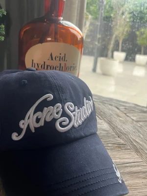 Mörkblå Acne Studios keps - Skriv innan köp!!         Snygg mörkblå keps från Acne Studios med vit broderad logga framtill och på skärmen. Klassisk böjd skärm och justerbar baksida. Tillverkad i bomullstyg som ger en avslappnad och trendig look.
