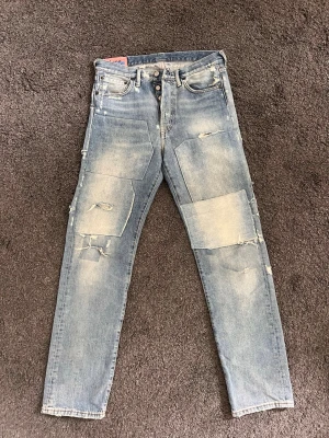 Patchade ljusblå jeans från Acne Studios - Säljer ett par ljusblå jeans från Acne Studios med stora patchade detaljer och slitningar framtill. Jeansen har raka ben, klassisk femficksmodell och knäppning med knappar. Materialet är denim i bomull och de har en trendig, avslappnad look. Jag är 182 och de sitter perfekt på mig, längdmässigt och på höfterna. Använda ca 10 gånger, ingen defekt eller något. Nypris ca 4500kr