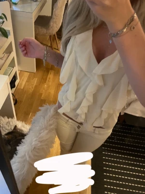 Vit blus med volanger och v-ringning - Supersöt kräm vit blus med djup v-ringning och volangdetaljer framtill. Blusen har korta ärmar och ett flowy fall som ger en romantisk vibe. Perfekt att styla med jeans eller kjol för en trendig look. Helt perfekt för skolavslutningen/examen eller vilken annan sommardag man vill bära denna vackra blus som passar perfekt till ett par jeansshorts😍 köpt förra året men har tyvärr bara kommit till andvänding 2 gånger, tror den är köpt för 200-350kr kommer ej ihåg.pris går diskuteras vid snabb affär!