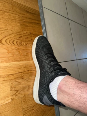 Svarta Adidas sneakers med vit sula - Svarta Adidas sneakers med mesh-överdel och vit sula. Skorna har låga skaft, klassisk snörning och diskret Adidas-logga på plösen och hälen. Perfekta för en avslappnad streetstyle-look.